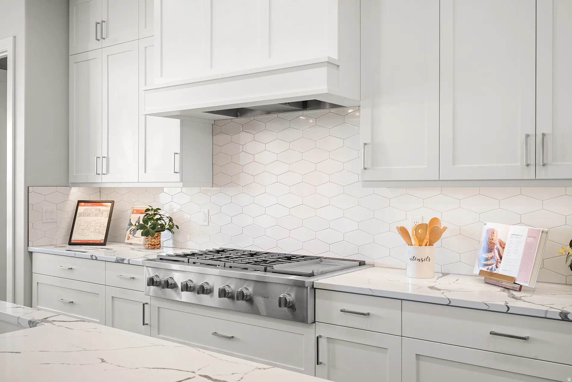 Gourmet kitchen featuring a stainless steel range, custom range hood, white shaker cabinetry, quartz countertops, and a white hexagonal tile backsplash