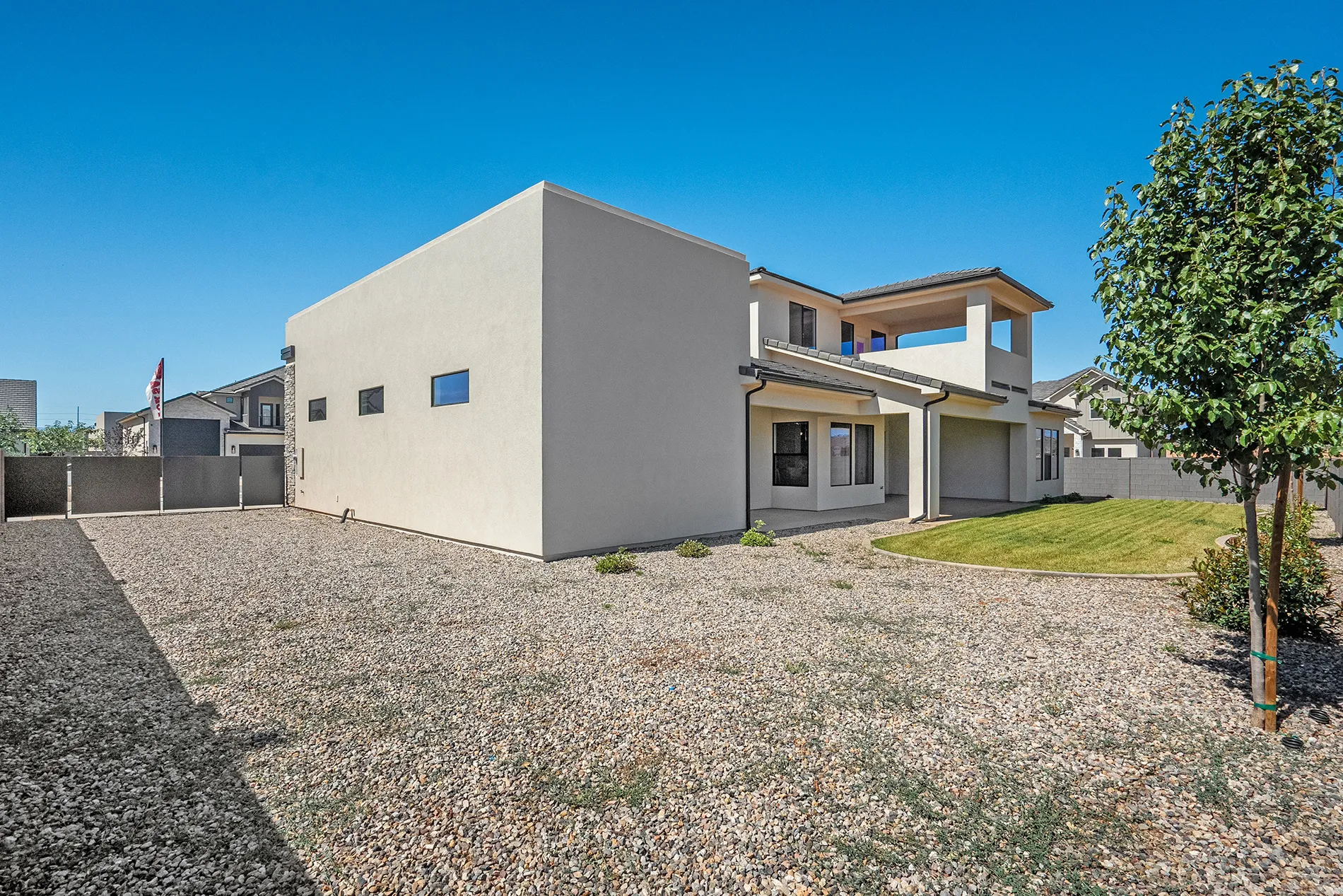 Contemporary stucco exterior featuring a covered patio, second-story balcony, horizontal windows, and a combination of gravel and manicured lawn landscaping