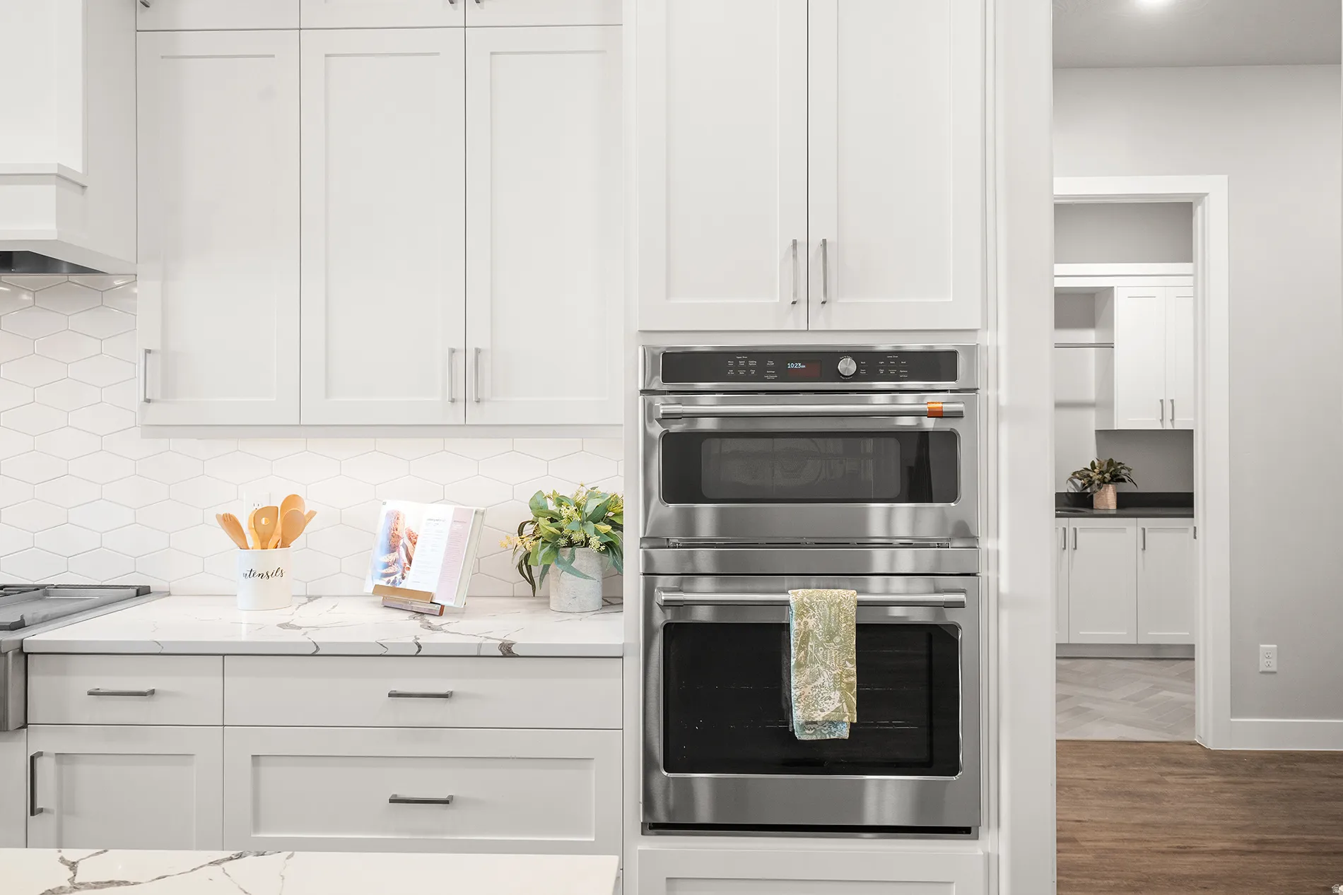 Modern kitchen featuring white shaker cabinetry, stainless steel double wall ovens, a quartz countertop, and a white hexagonal tile backsplash