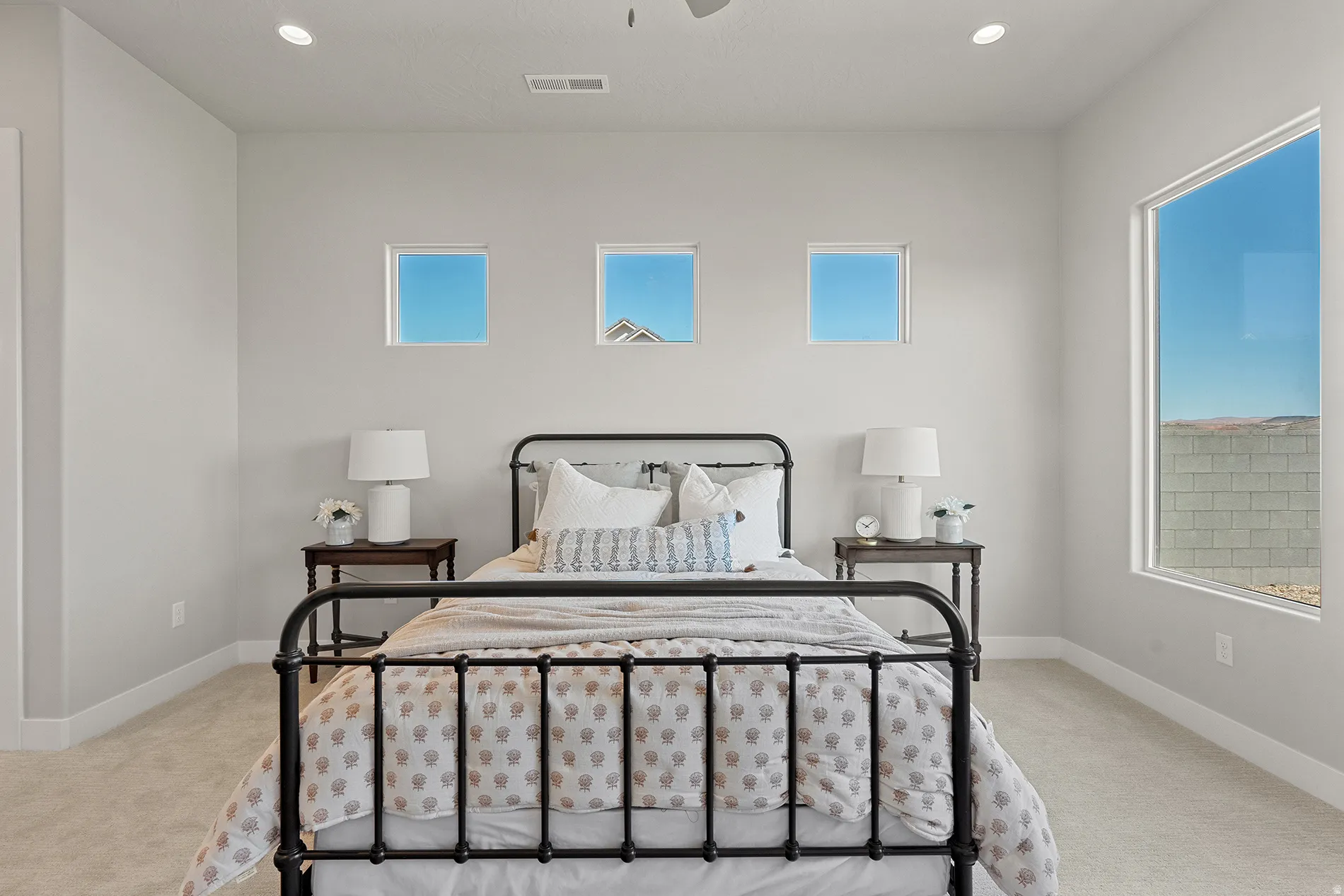 Primary Expansive bedroom featuring light grey walls, recessed ceiling lighting, a large picture window, and three square accent windows