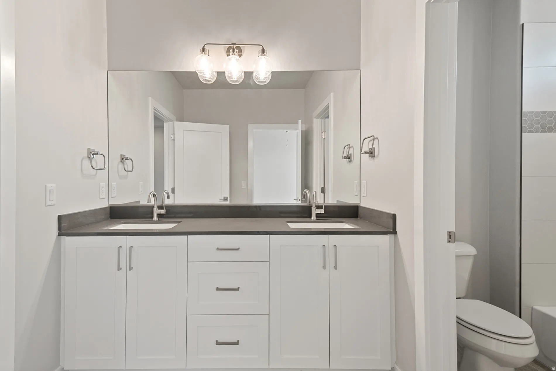 Dual sink vanity featuring white cabinetry, a dark countertop, and brushed nickel hardware