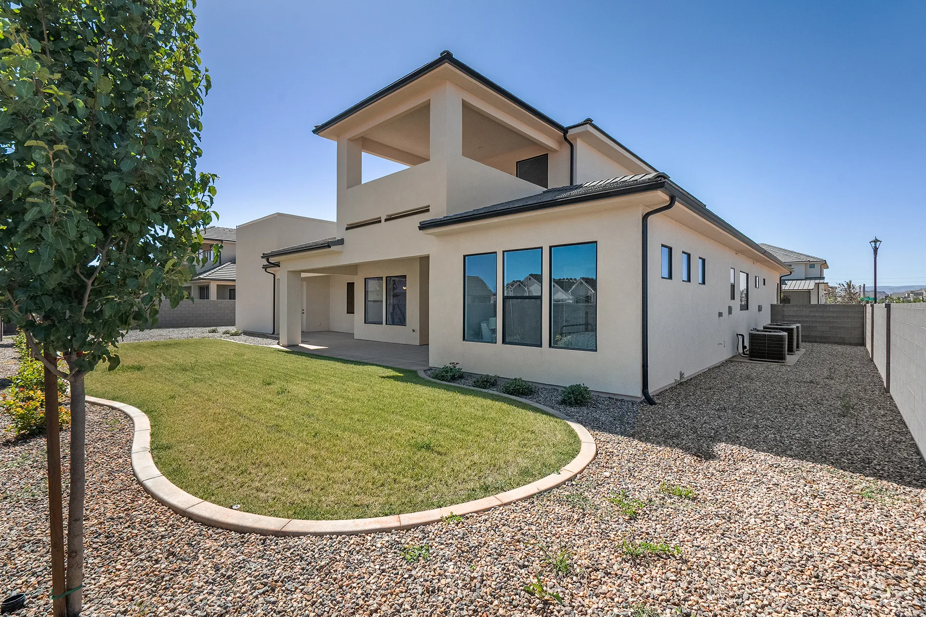 Exterior stucco residence with a covered patio, second-story balcony, and a landscaped backyard featuring a grass lawn and gravel areas