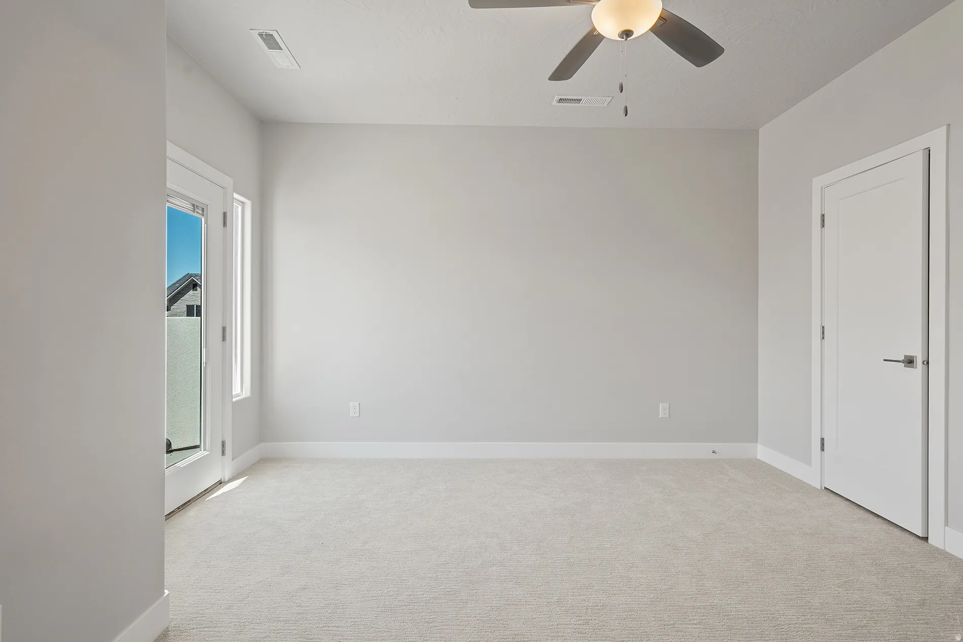 Carpeted room with a ceiling fan light fixture, white baseboards, and a glass-paneled door