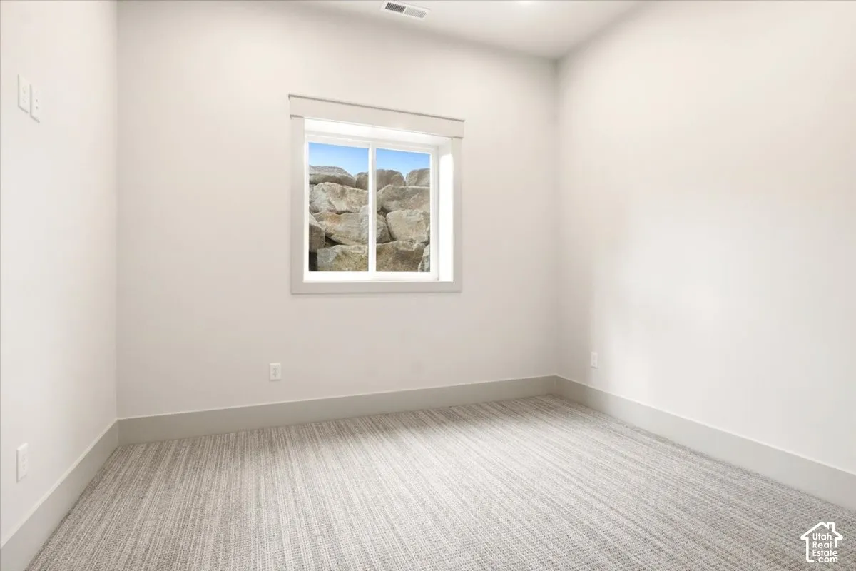 Neutral interior space featuring textured wall-to-wall carpeting, crisp white walls, and a recessed window with an exterior rock wall exposure