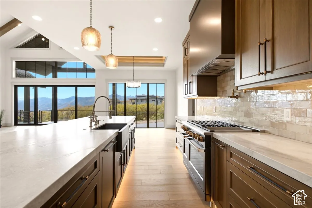 Kitchen featuring custom wood cabinetry, expansive stone countertops, a farmhouse-style sink, and a professional-grade gas range with a matching range hood