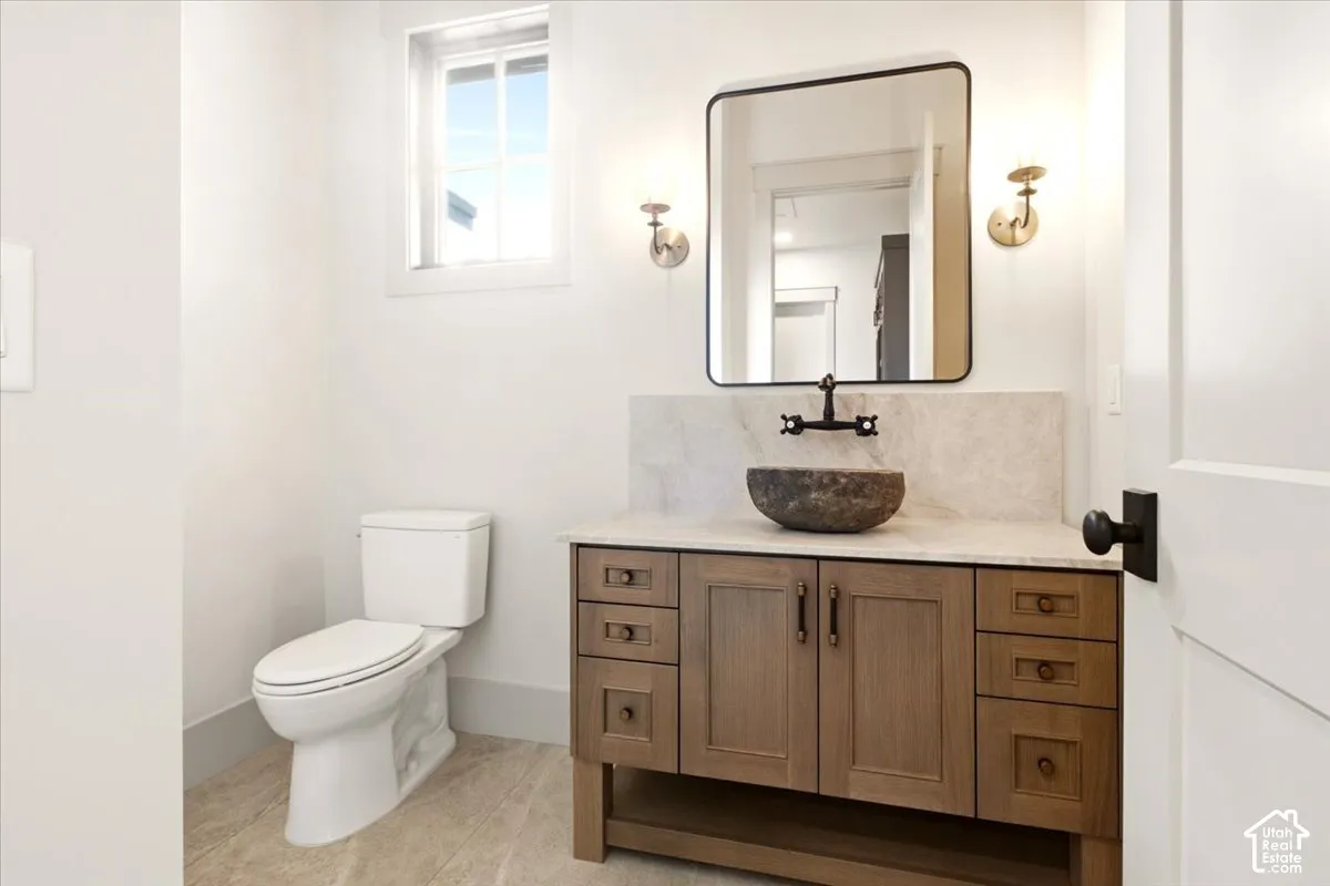 Custom wood-finish vanity with a stone vessel sink, wall-mounted faucet, neutral stone backsplash, and rectangular wall mirror with rounded corners