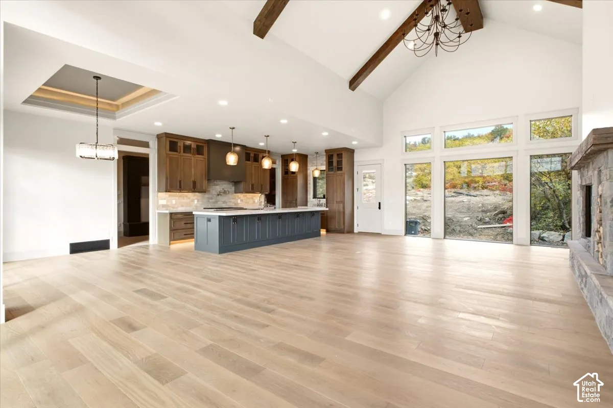 Open-concept interior featuring vaulted ceilings with exposed wood beams, wood-finish flooring, a kitchen island with custom cabinetry, and a stone-accented fireplace