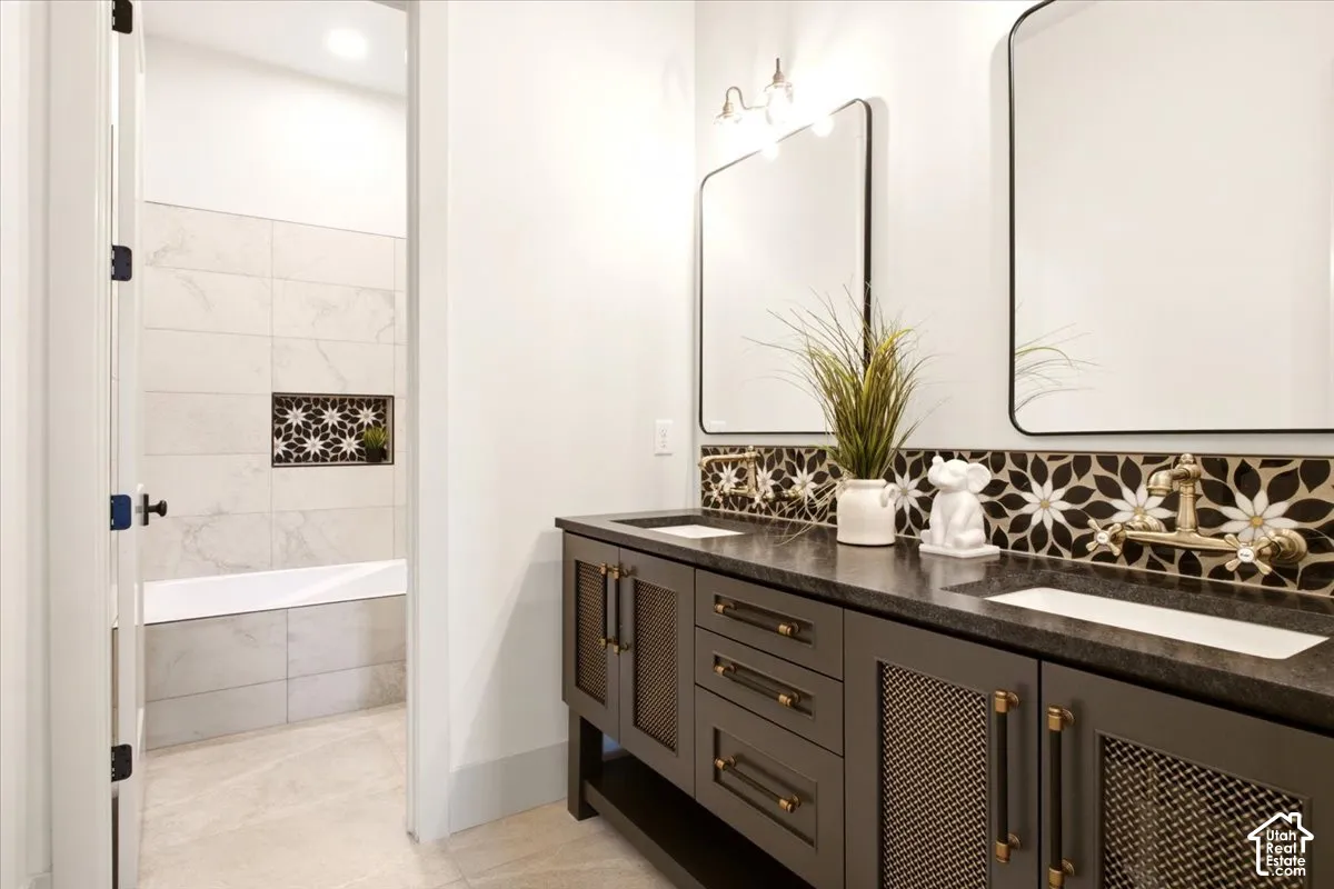 Dual-sink vanity featuring charcoal-toned cabinetry, metallic mesh door inserts, brass-finish hardware, and a dark stone countertop