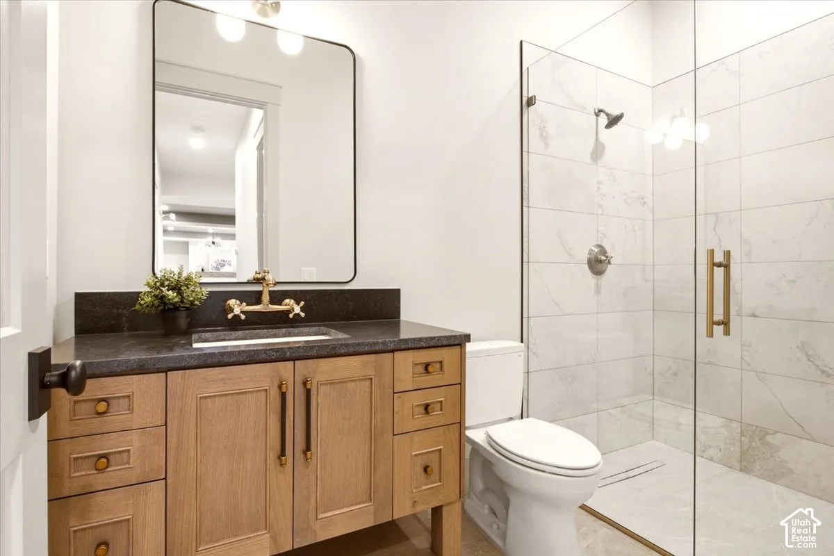 Custom wood-finish vanity with a dark stone countertop, brass wall-mounted faucet, rectangular mirror with a metal frame, and a walk-in shower featuring glass doors