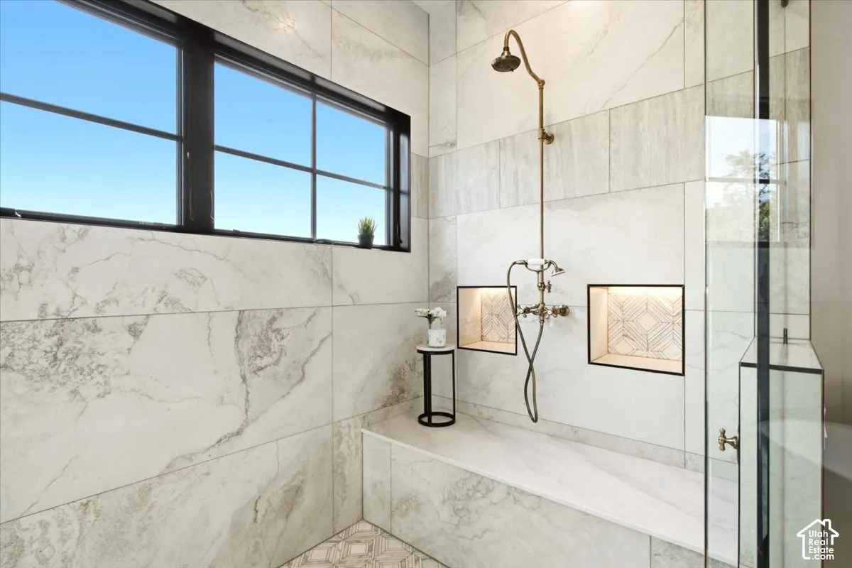 Walk-in shower featuring floor-to-ceiling stone-patterned tile, a built-in stone bench, dual recessed wall niches, an antique-finish rainfall showerhead, and a black-framed window showcasing the views