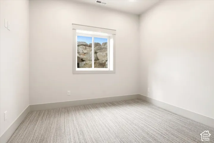 Neutral interior space featuring textured wall-to-wall carpeting, crisp white walls, and a recessed window with an exterior rock wall exposure