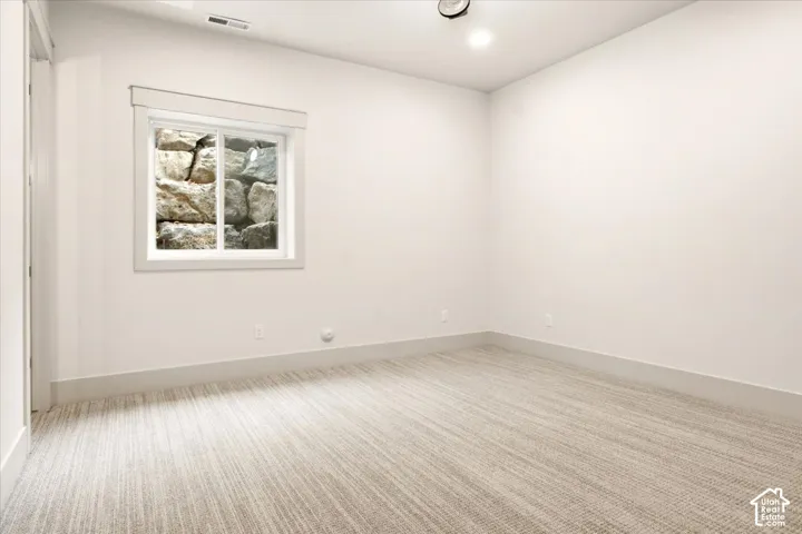 Neutral-toned wall-to-wall carpeting, crisp white walls, and a sliding window featuring a stone retaining wall backdrop