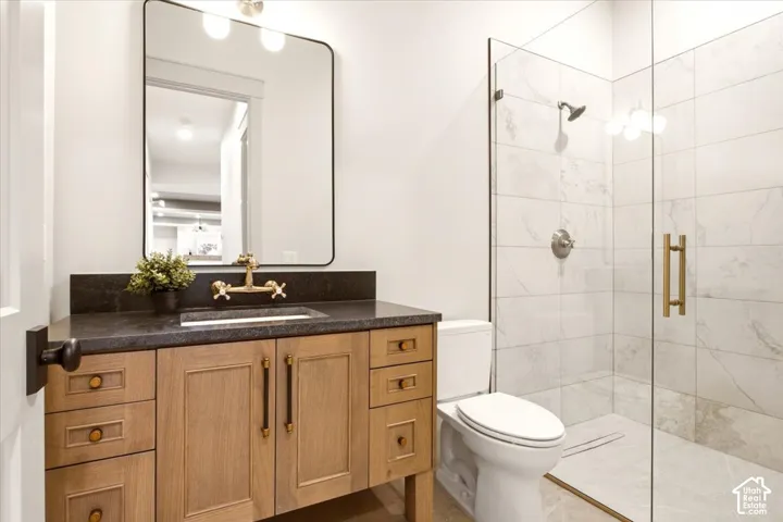 Custom wood-finish vanity with a dark stone countertop, brass wall-mounted faucet, rectangular mirror with a metal frame, and a walk-in shower featuring glass doors