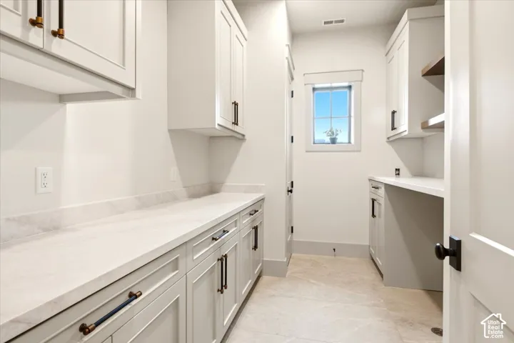 Basement laundry room featuring built-in cabinetry with open shelving, integrated desk space, stone-finish countertops, and tiled flooring