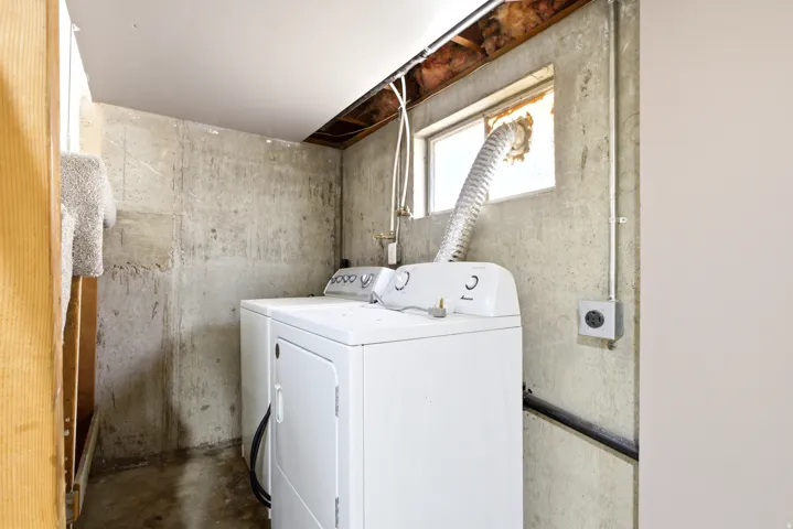 Laundry area with a washer and dryer unit, exposed concrete walls, and a window for natural light