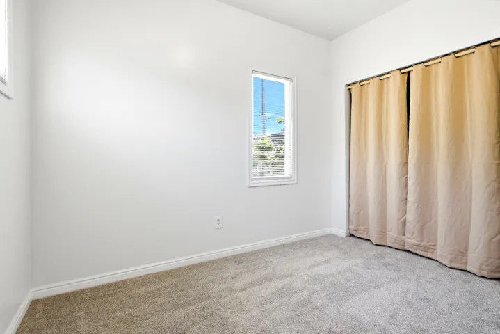 Carpeted room featuring a single window with blinds, white walls, and baseboards