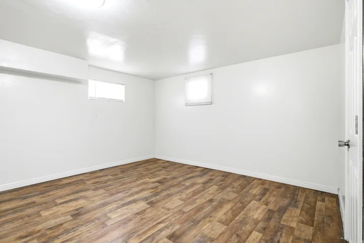 Spacious room featuring wood-finish flooring, white walls, and bright overhead lighting
