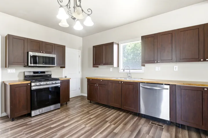 Kitchen featuring dark wood-finish cabinetry, light wood-finish countertops, stainless steel appliances, and wood-finish flooring