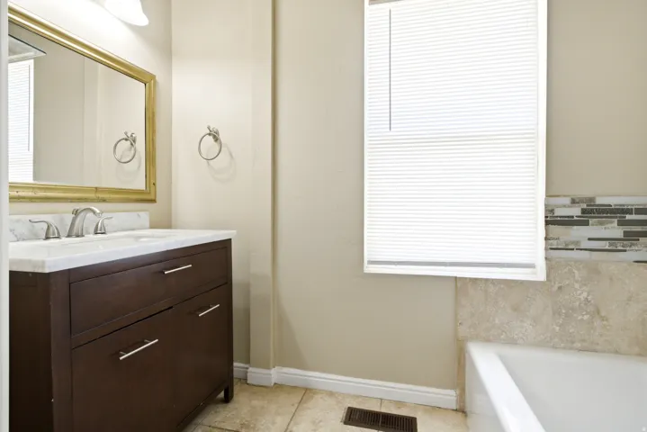 Bathroom featuring a dark wood-finish vanity with a white countertop and undermount sink, brushed nickel faucet, and a gold-framed mirror