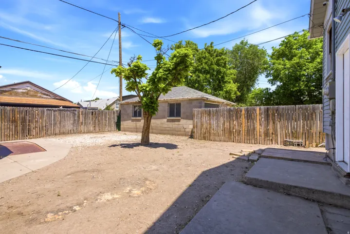 Enclosed backyard featuring a concrete patio, wood fencing, and a mature tree