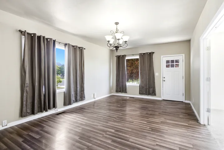 Spacious living area featuring wood-finish flooring, neutral wall tones, and a multi-light chandelier