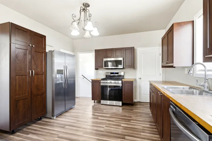 Kitchen featuring wood-finish flooring, dark wood cabinetry, stainless steel appliances, and light wood countertops