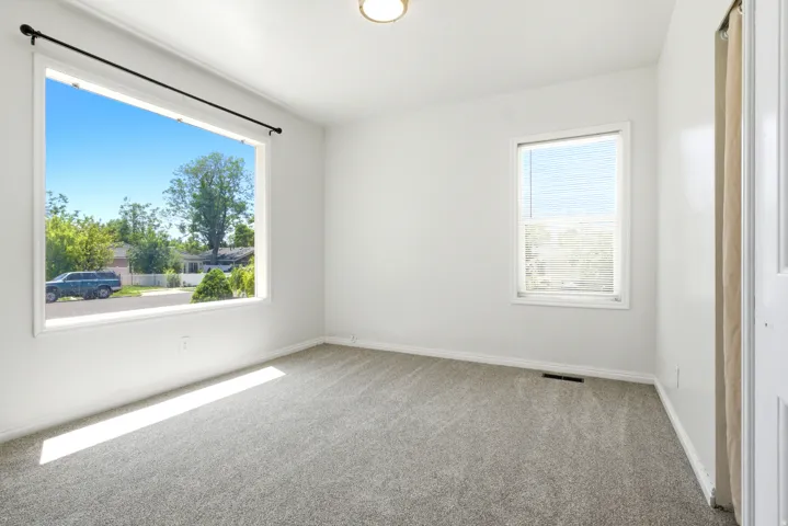 Bright room featuring a large picture window, a secondary window with blinds, light-toned carpeting, white painted walls, and a ceiling-mounted light fixture