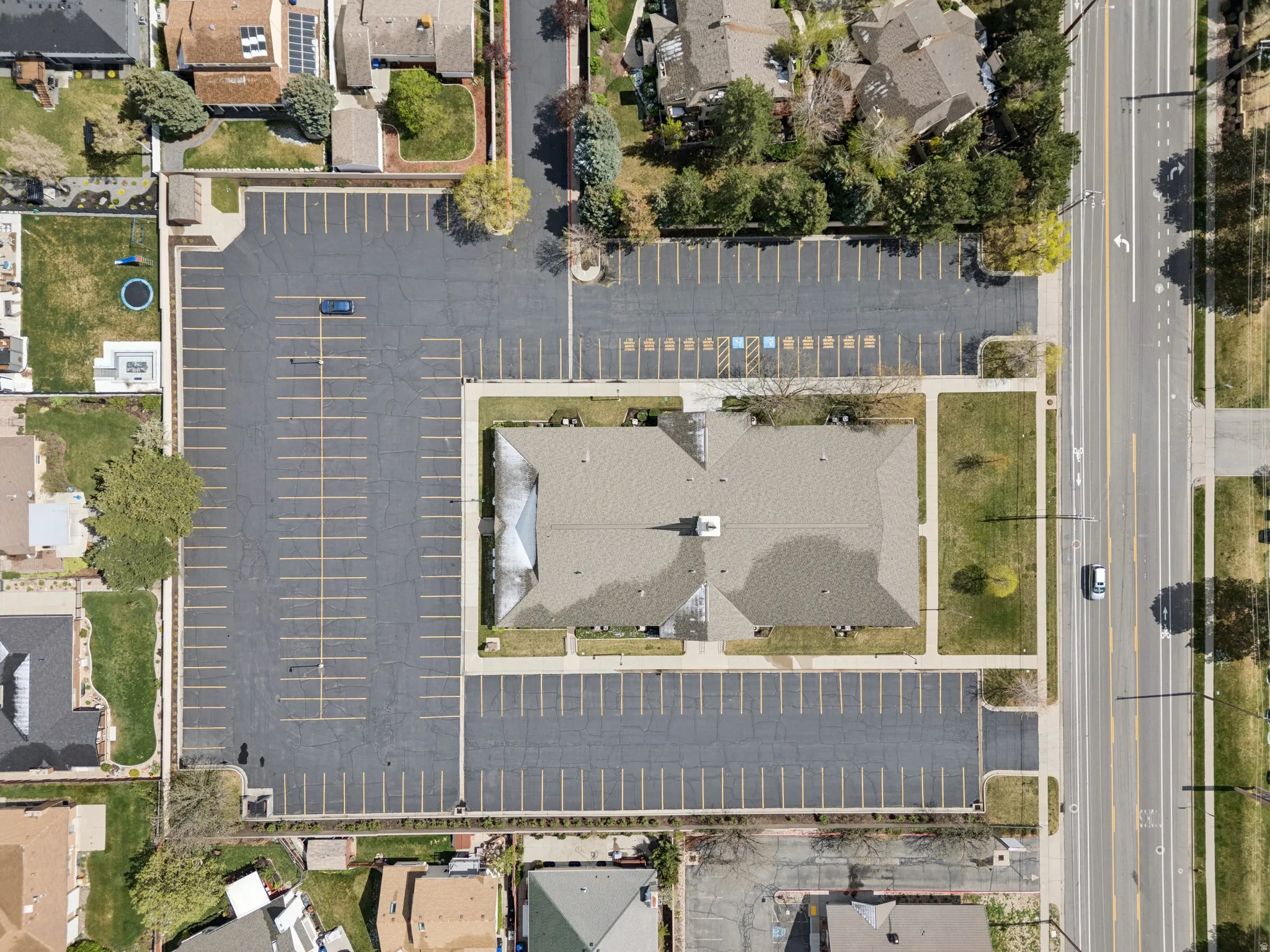 Expansive commercial property featuring a central building with a shingled roof, surrounded by a large asphalt parking lot with multiple marked spaces.