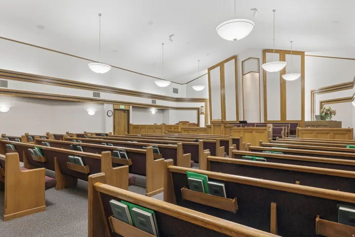 Spacious interior featuring multiple rows of built-in wooden seating with upholstered backs, integrated lighting, recessed wall panels with wood trim, and a high vaulted ceiling with pendant and wall sconce lighting.