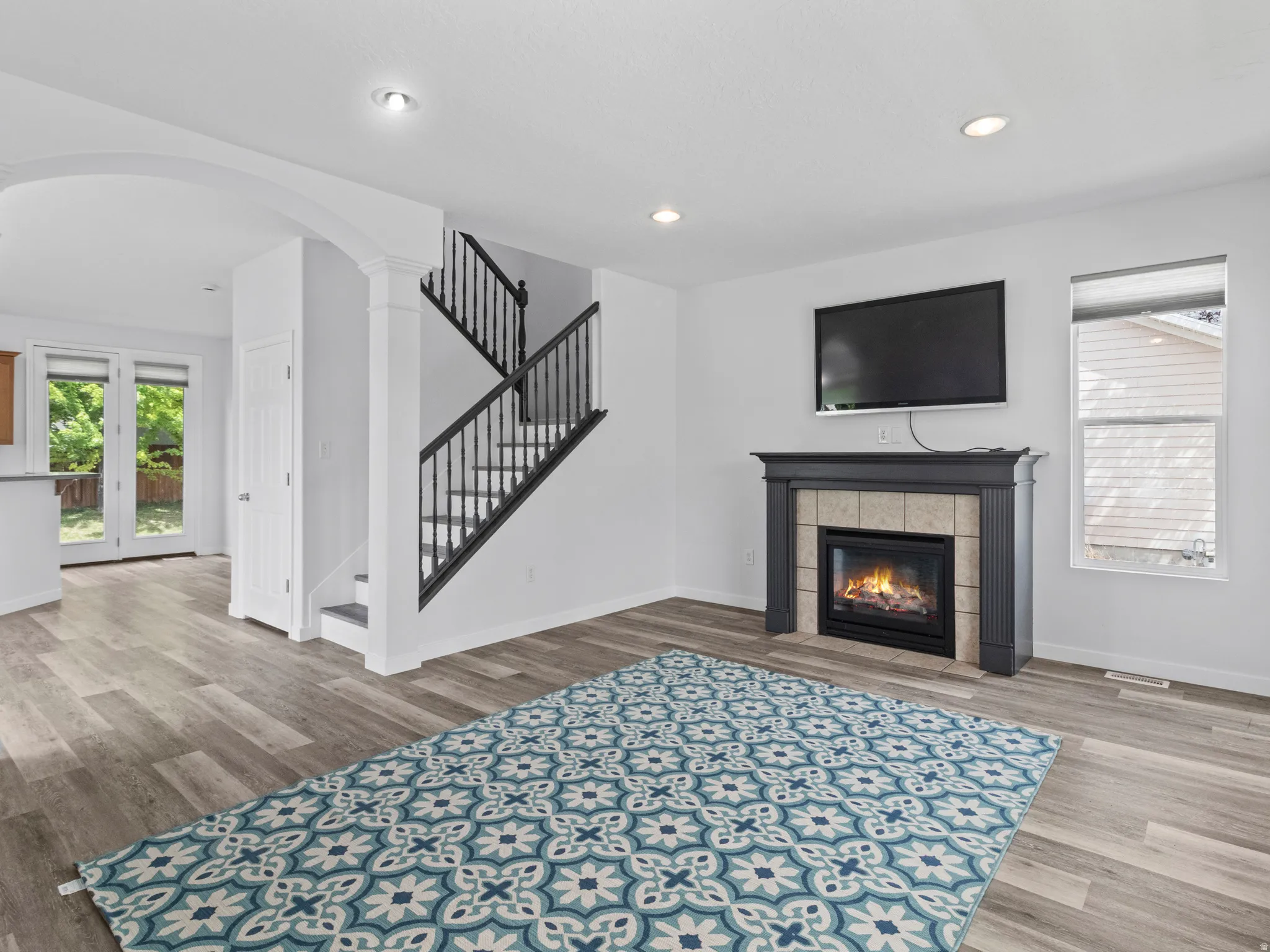 Spacious living area featuring light wood-finish flooring, a contemporary fireplace with a tiled surround and dark wood mantel, and recessed lighting