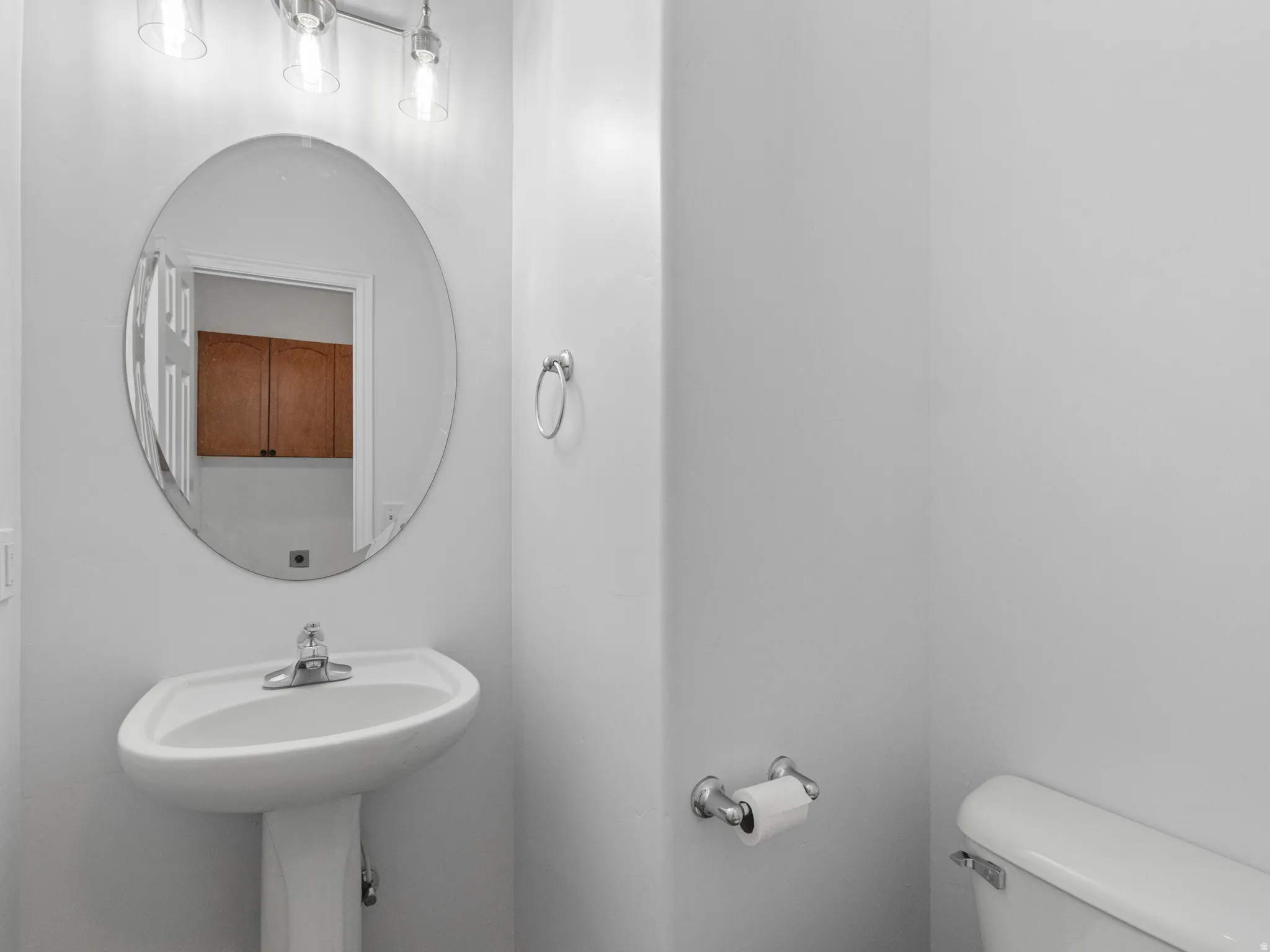 Powder room featuring a pedestal sink with chrome faucet, oval frameless mirror, and a three-light vanity fixture