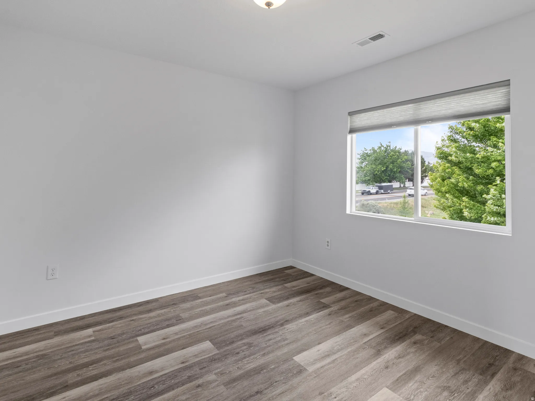 Room featuring wood-finish flooring, white baseboards, and a window with blinds