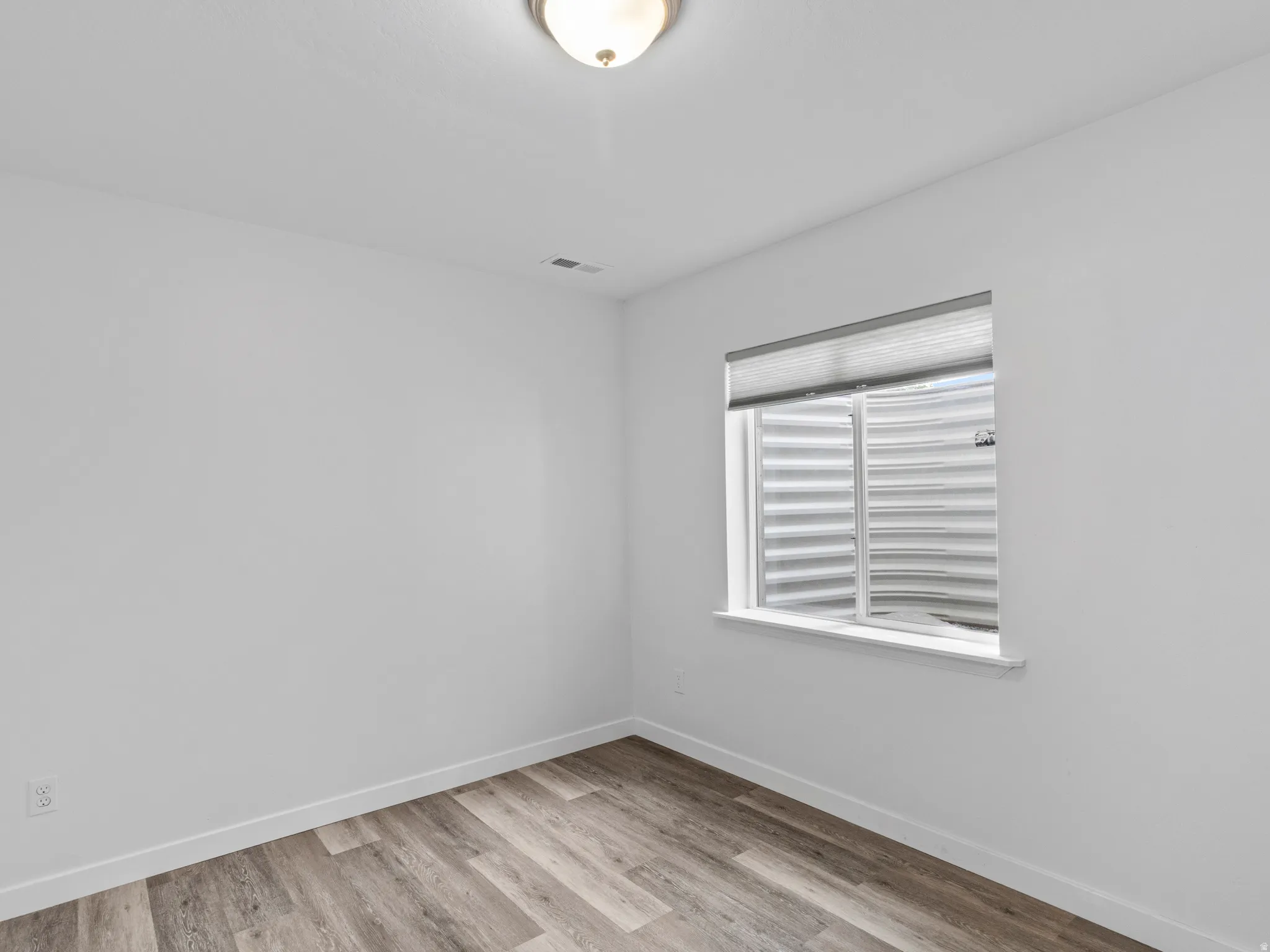 Room featuring a window with privacy blinds, light wood-finish flooring, white baseboards, and a flush-mount ceiling light fixture