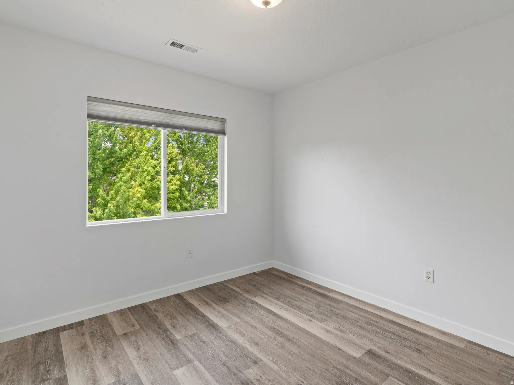 Bright interior space featuring wood-finish flooring, white walls, and a large window with roller shades