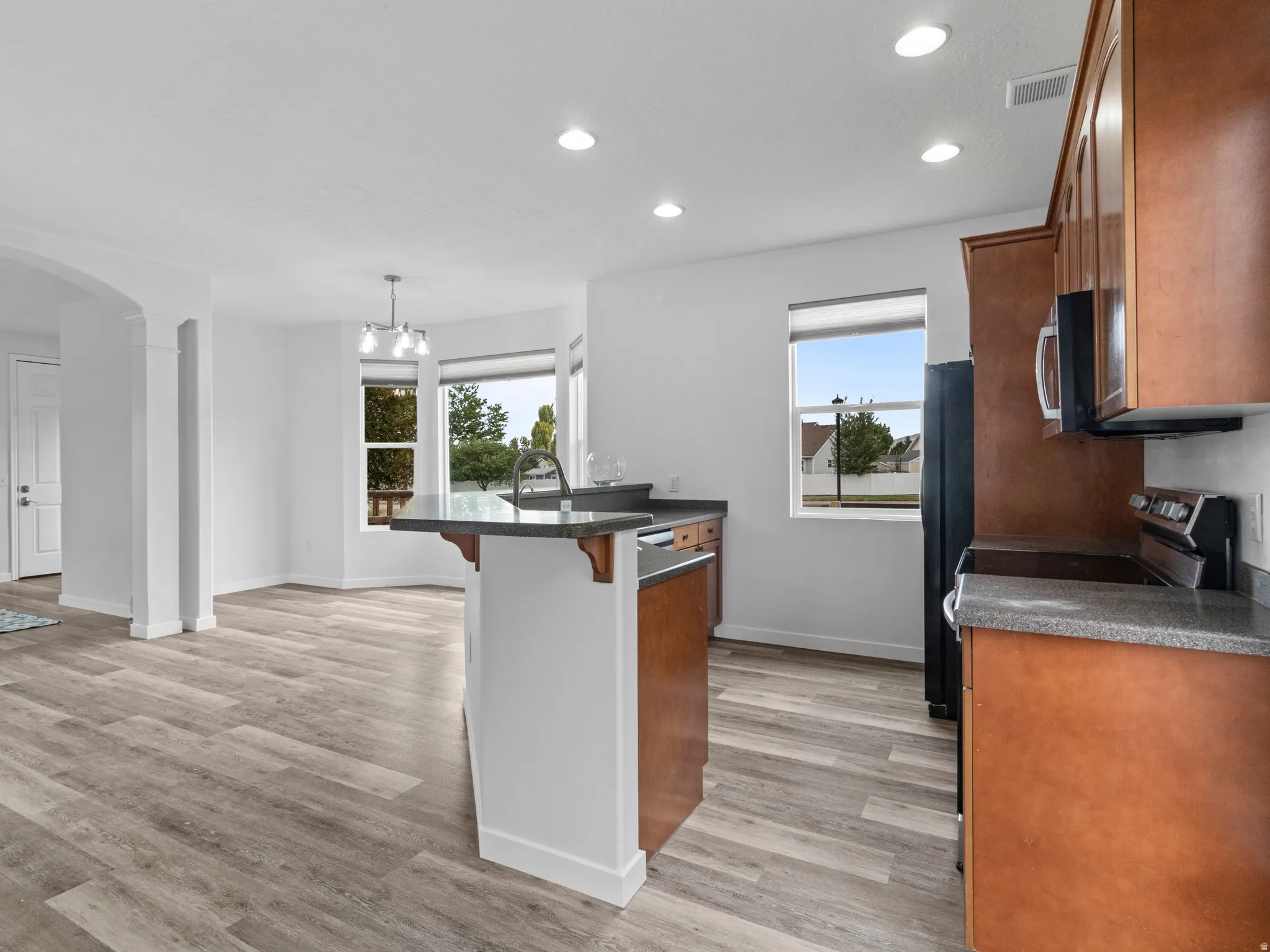 Kitchen featuring an island with a sink, wood-finish flooring, recessed lighting, and a bay window