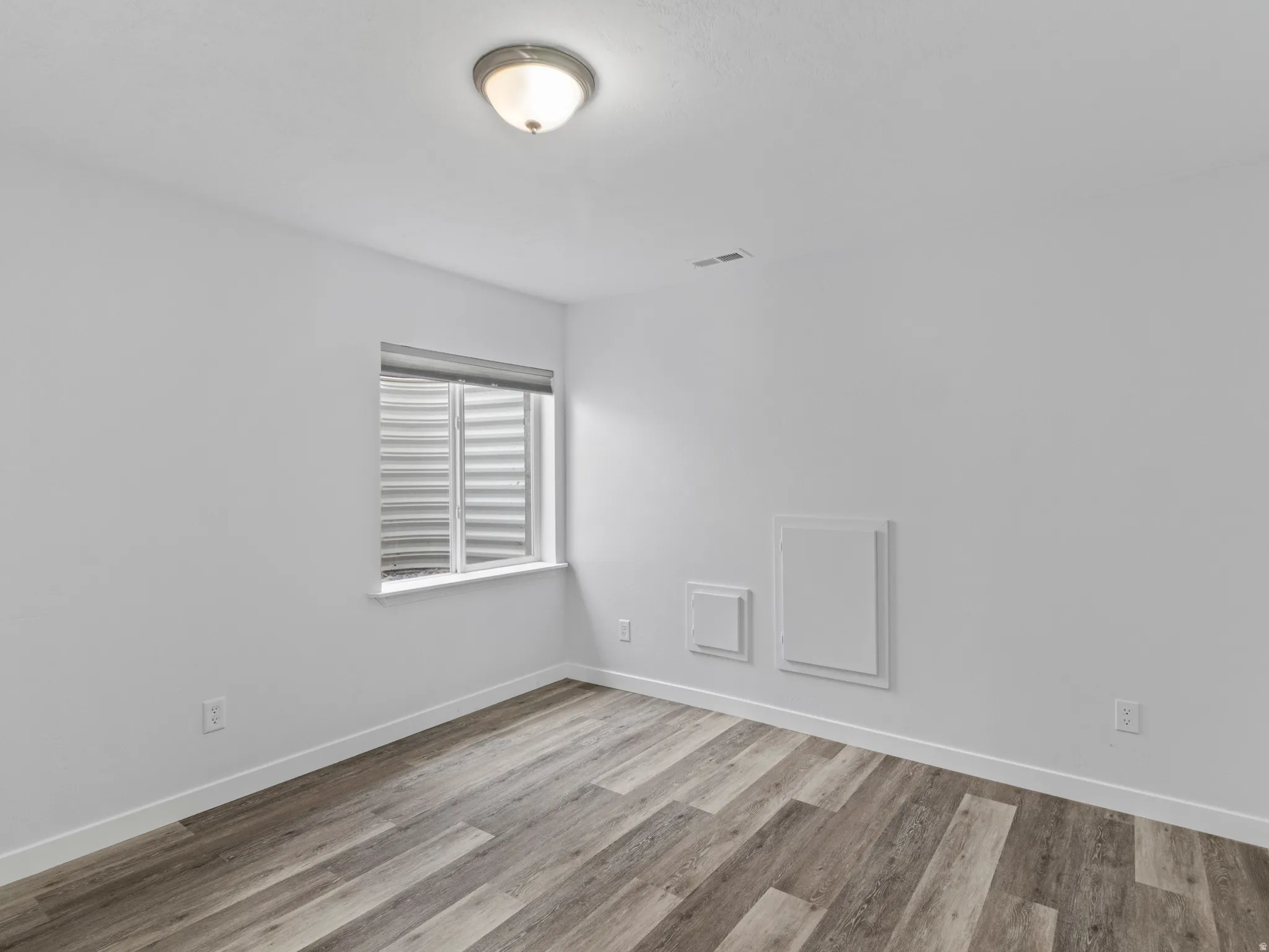 Room featuring wood-finish flooring, white baseboards, and a window with a blind