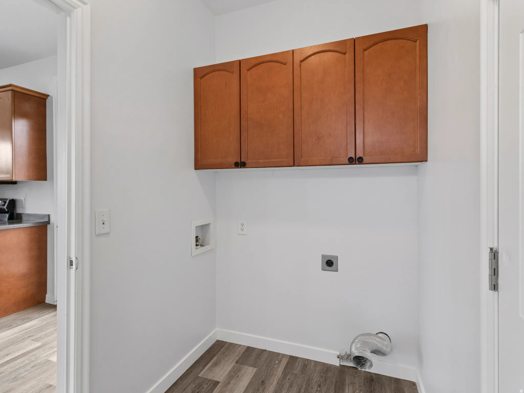 Laundry area featuring wood-finish flooring, white walls, and built-in upper cabinetry with arch-panel doors and black hardware