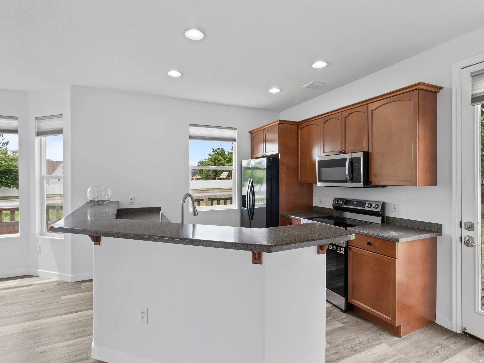Kitchen featuring a large island with a sink, wood-finish flooring, recessed lighting, wood cabinetry, and stainless steel appliances