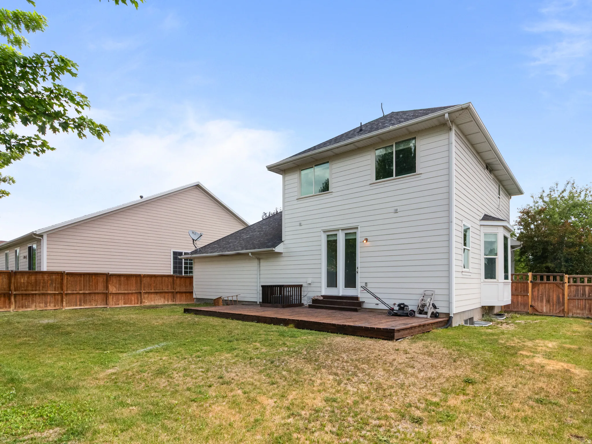 Expansive backyard featuring a wood deck, white vinyl siding, a bay window, double glass doors, and privacy fencing