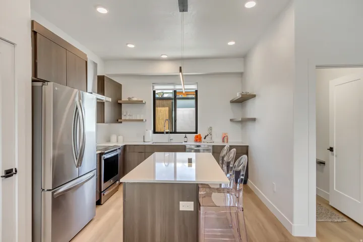 Contemporary kitchen featuring wood-finish cabinetry, stainless steel appliances, a center island with countertop seating, recessed lighting, and light wood-finish flooring