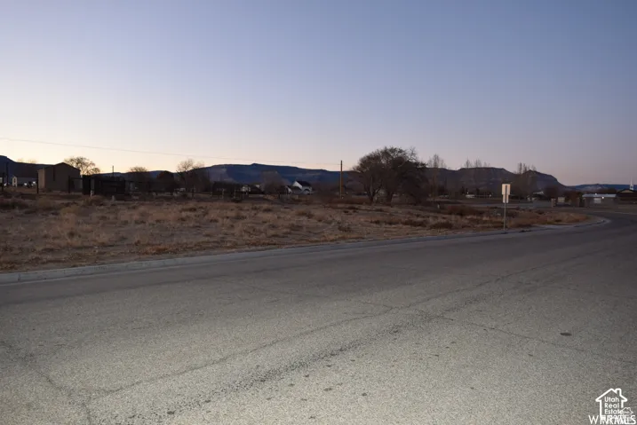 Paved road frontage with an expansive, undeveloped lot featuring dry vegetation and distant mountainous terrain