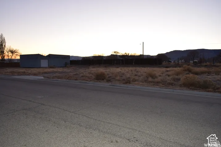 Expansive undeveloped land featuring a paved road frontage, mature trees, and two storage structures with garage doors