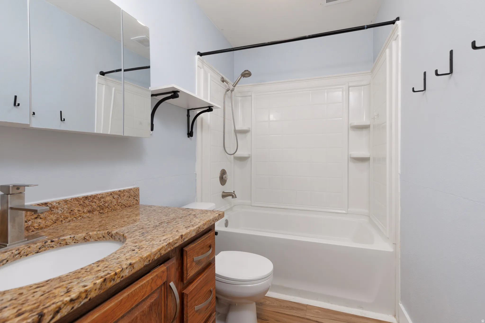 Bathroom featuring a white bathtub with a shower kit, a dark wood-finish vanity with a stone countertop and integrated sink, a mirrored medicine cabinet, and wood-finish flooring