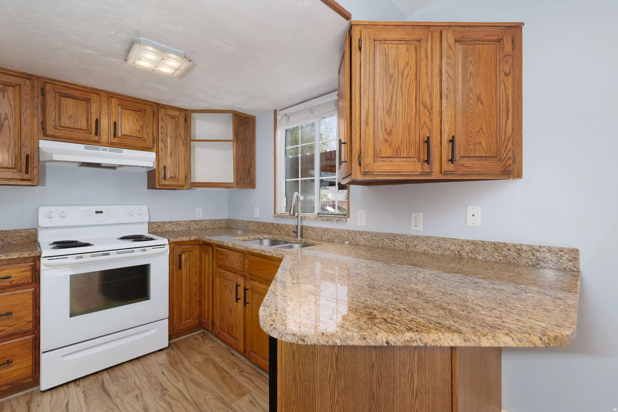 Kitchen featuring wood-finish cabinetry, speckled countertops, and a white electric range with matching range hood