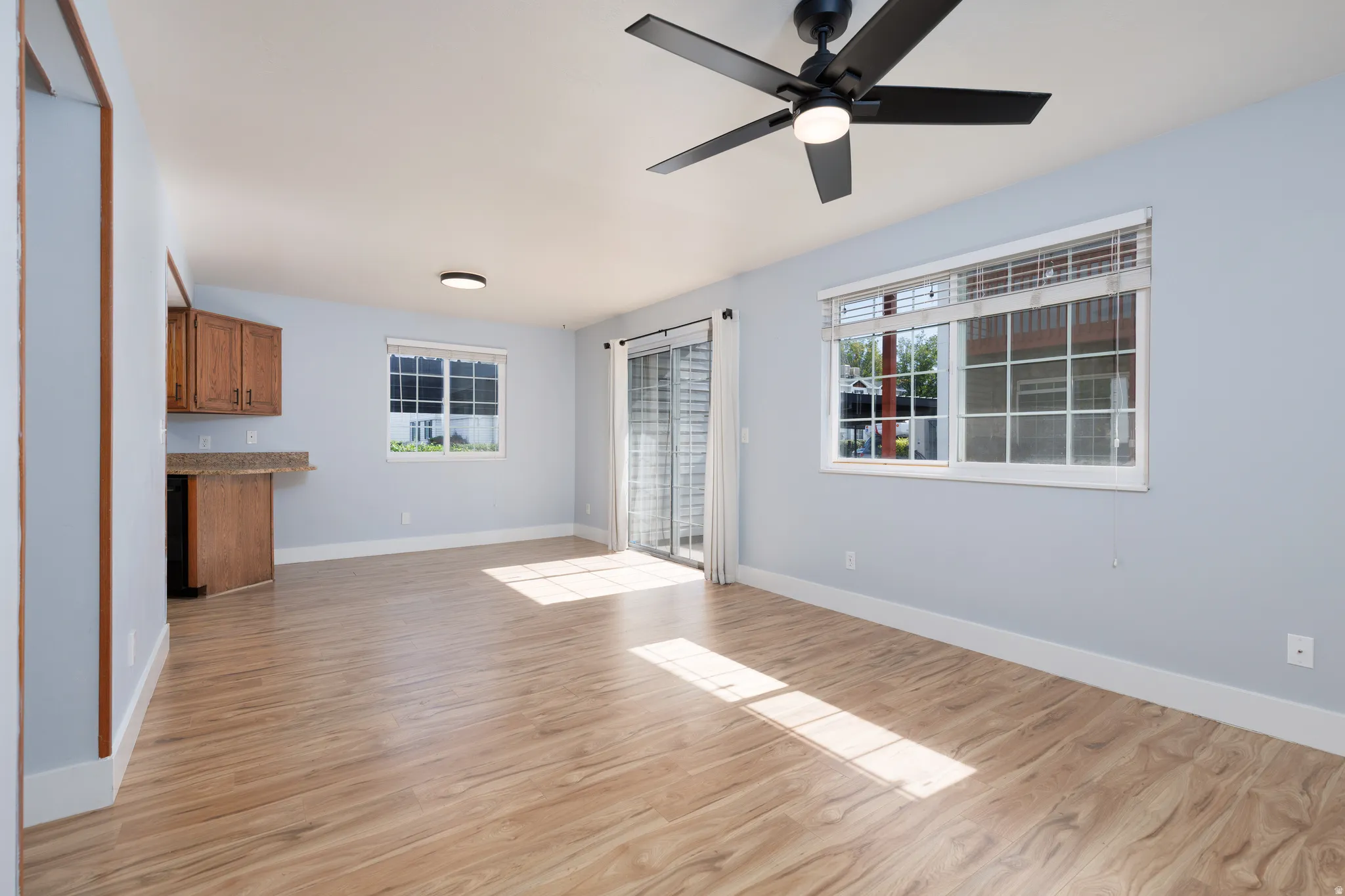 Spacious room featuring wood-finish flooring, a contemporary ceiling fan with integrated lighting, and light blue walls