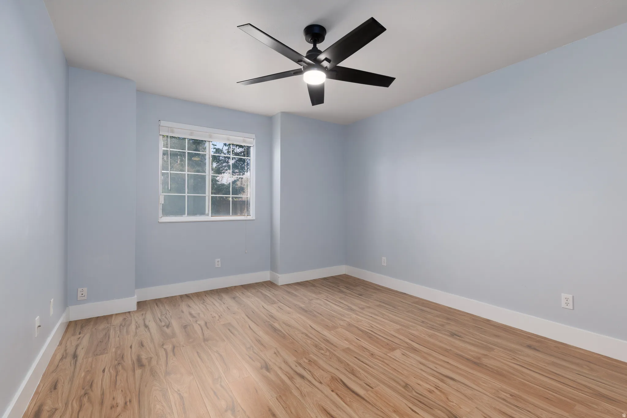 Spacious room featuring wood-finish flooring, light blue walls, and white baseboards