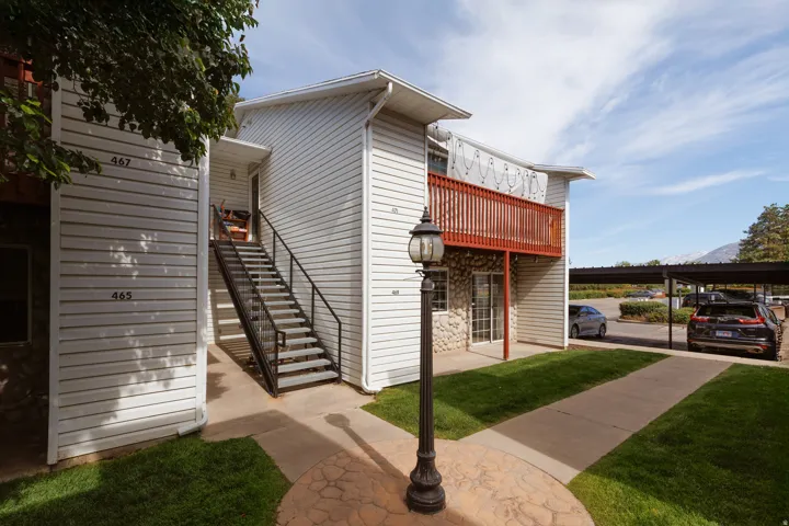 Exterior building featuring white siding, a red-railed balcony, and a ground-level patio with stone veneer