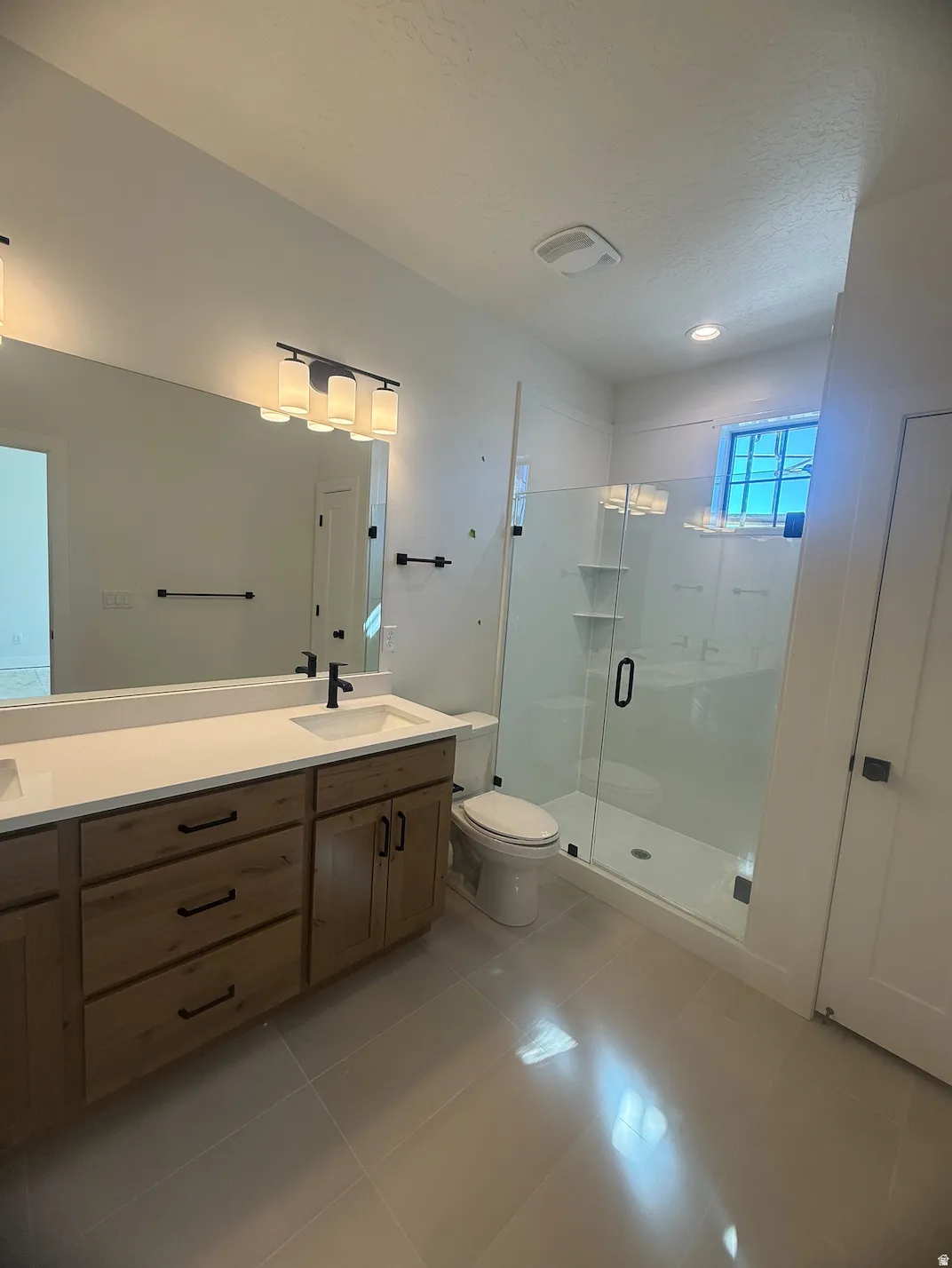 Bathroom featuring a dual vanity with light wood-finish cabinetry, white countertops, and matte black fixtures