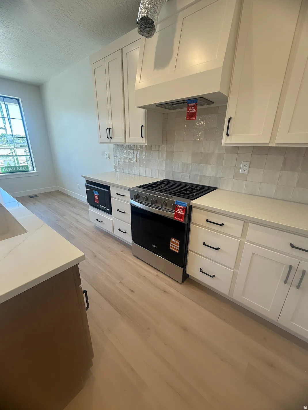 Modern kitchen featuring white shaker cabinetry with matte black hardware, light-toned wood-finish flooring, white countertops, a mosaic tile backsplash, and stainless steel appliances