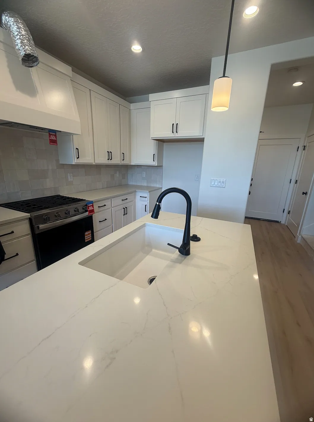 Kitchen island with an undermount sink, quartz countertop, matte black pull-down faucet, and pendant lighting